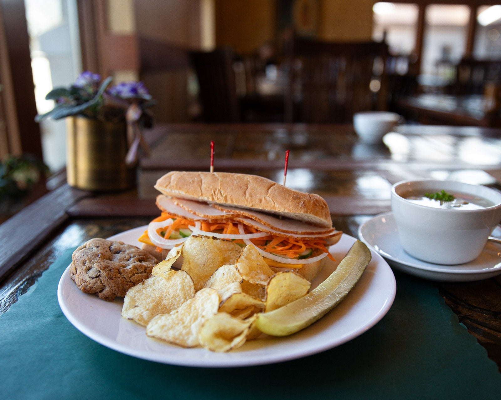 Plated sandwich with chips and a bowl of soup on a table.