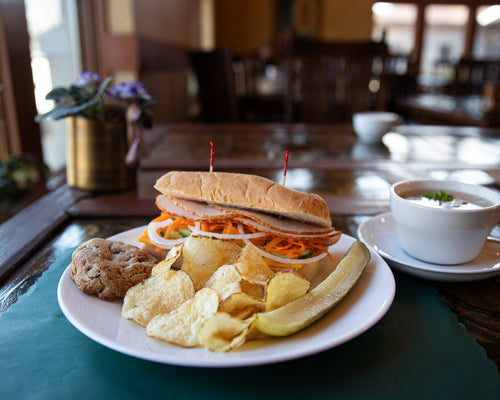 Plated sandwich with chips and a bowl of soup on a table.