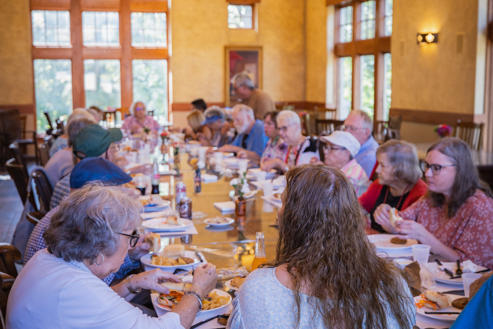 Group of people enjoying a Culina Meal at a long table in a large room with windows.