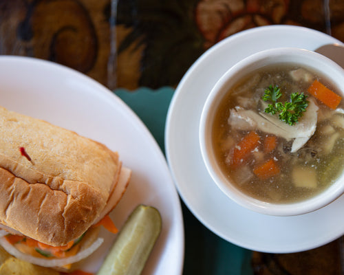 Bowl of soup with vegetables and a sandwich on a plate.